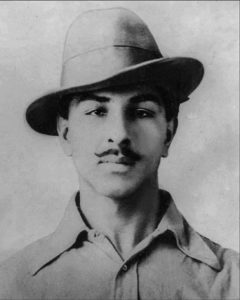 A photograph of Bhagat Singh, a young man with a short mustache. He is wearing a large fedora and a white collared shirt. 