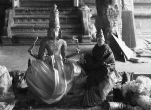 a statue holds up candles and other offerings around it