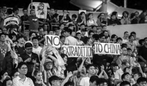 a crowd gathers, with signs saying "no extradition to china"